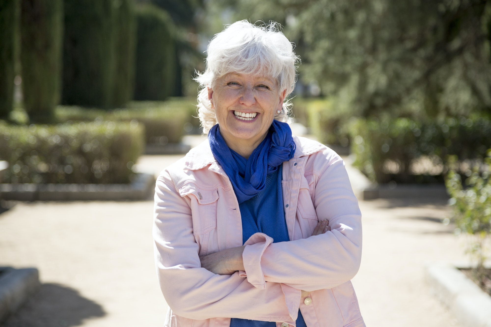 middle-aged woman with white hair looking at camera with arms crossed in park